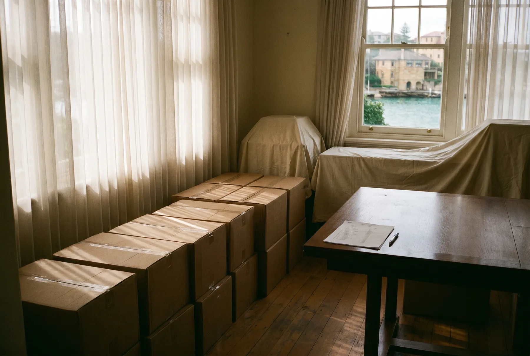 A quiet room with sealed cartons in rows, dust-sheeted furniture, and an inventory list on the table