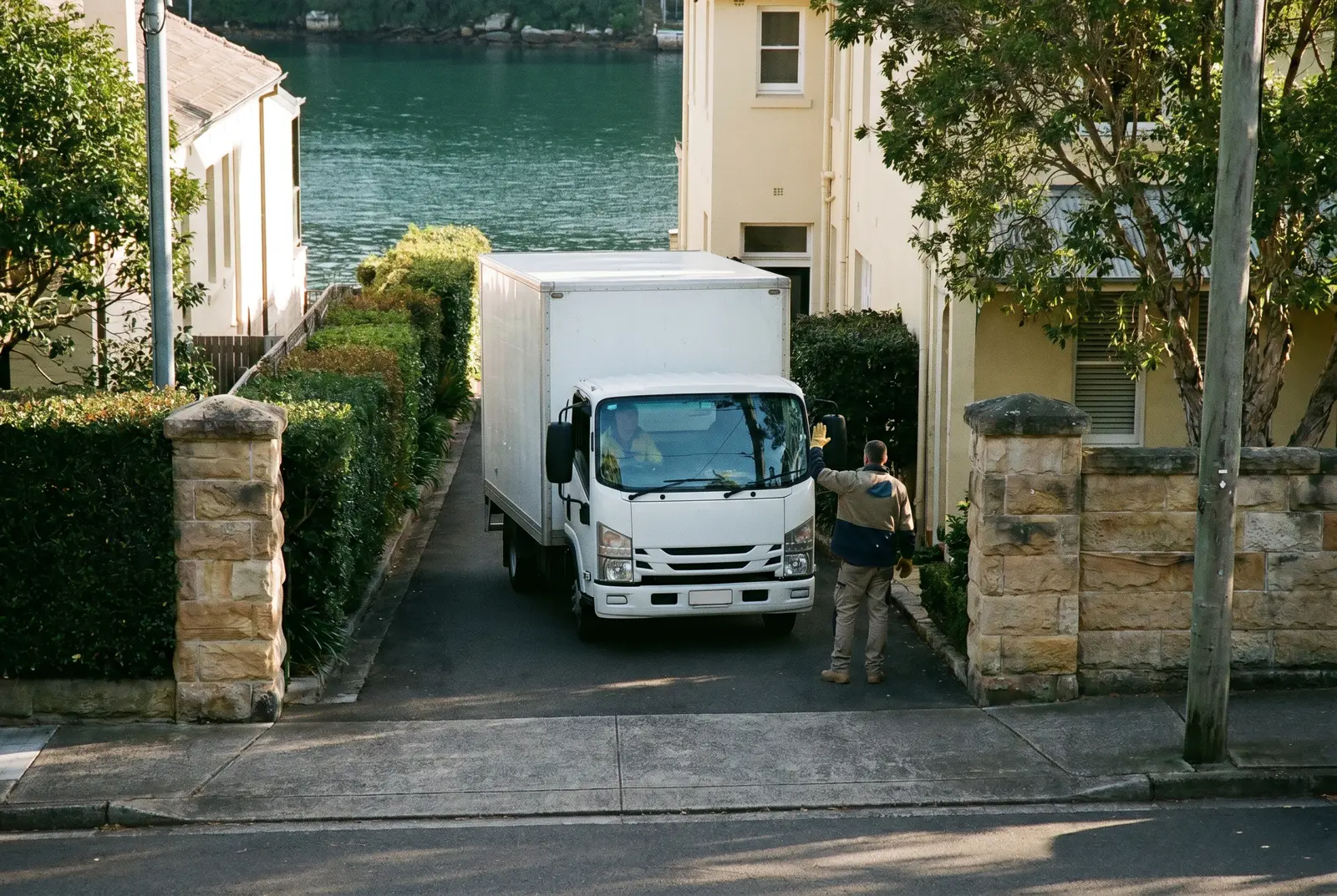 A compact removal truck reversing into a narrow Vaucluse driveway with a crew member guiding it